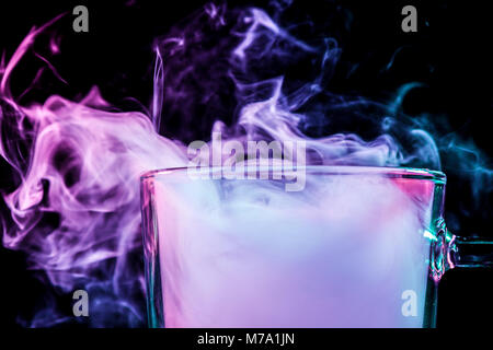Close up di un vetro trasparente per la birra riempita con un cloud da un rosa vape fuma e sorge su un isolato nero lo sfondo Foto Stock