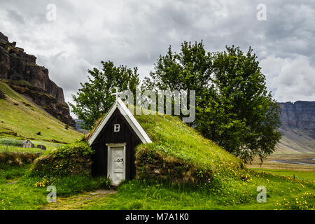 Islandese tradizionale chiesa di tappeto erboso ricoperto di erba, alberi e rocce dello sfondo vicino Kalfafell vilage, Sud Islanda Foto Stock