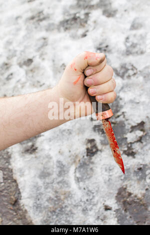 Sporco mano d'uomo con un coltello insanguinato contro lo sfondo della neve Foto Stock