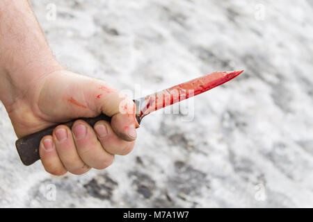 Sporco mano d'uomo con un coltello insanguinato sul terreno con la neve sullo sfondo Foto Stock