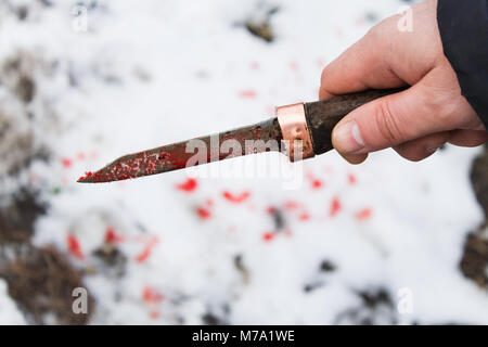 Mano d'uomo con un coltello insanguinato close-up su uno sfondo sfocato Foto Stock