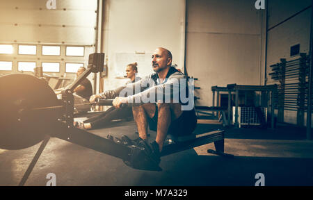 Montare uomo maturo esercitando su vogatori durante una classe di allenamento in palestra Foto Stock