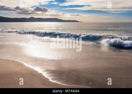 Le onde che si infrangono a spiriti Bay (Piwhane) con Cape Reinga a distanza, Isola del nord, Nuova Zelanda Foto Stock