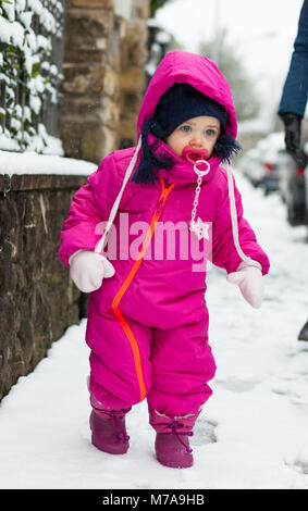 Toddler adorabile bambina in un magenta tuta da neve giocando sulla neve. Foto Stock