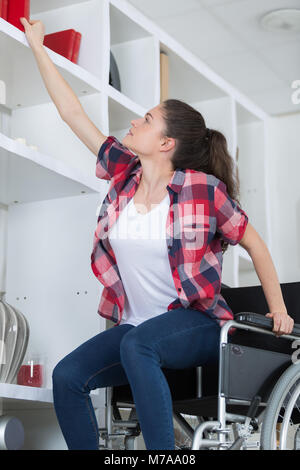 Donna disabile cercando di ottenere il libro la sedia a rotelle in soggiorno Foto Stock