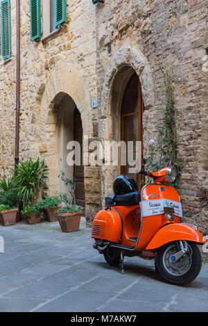 Arancione scooter a motore nella parte anteriore della facciata in pietra, Europa, Italia, Toscana, San Quirico d'Orcia Foto Stock