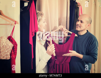 Donna sorridente medicazione in changeroom del negozio di abbigliamento, marito in attesa Foto Stock