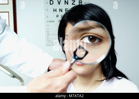 Close-up di un medico che la mano che tiene una lente di ingrandimento nella parte anteriore di una giovane donna di occhio Foto Stock