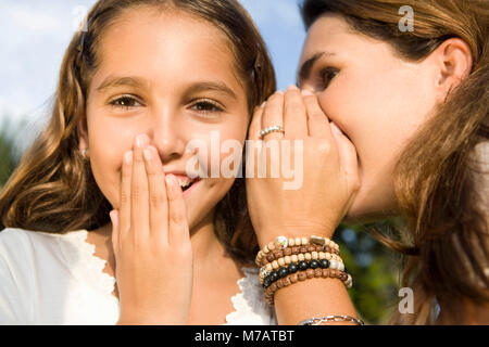 Close-up di una metà donna adulta whispering in sua figlia l orecchio Foto Stock
