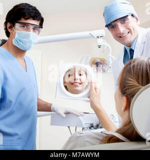 Donna che guarda in specchio con due maschio dentisti in una clinica Foto Stock