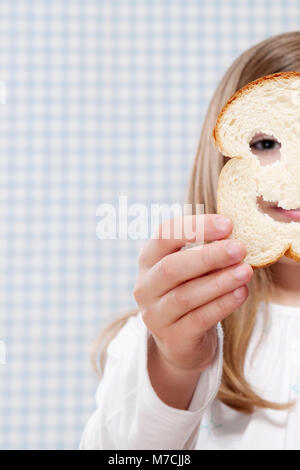 Ragazza con una fetta di pane nella parte anteriore del suo viso Foto Stock