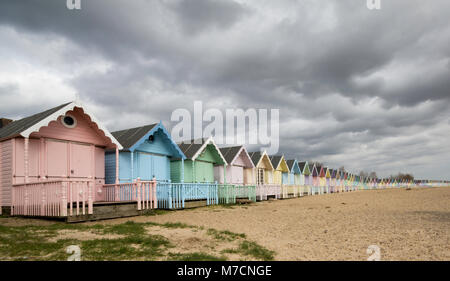 Il pastello colorato capanne sulla spiaggia a East Mersea, Essex con una drammatica cloudscape sopra. Foto Stock