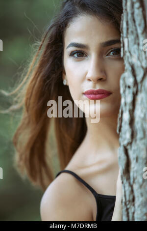 Bella giovane donna nascondersi dietro a un albero Foto Stock