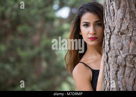 Bella giovane donna nascondersi dietro a un albero Foto Stock