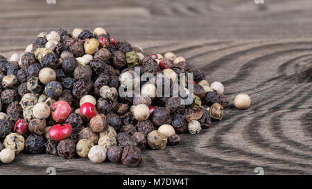 Close-up di peppe essiccato mix su una tabella. Piper nigrum. Bellissimo pelo colorati di diversa pepe i calli sul sfocata sullo sfondo di legno. Foto Stock