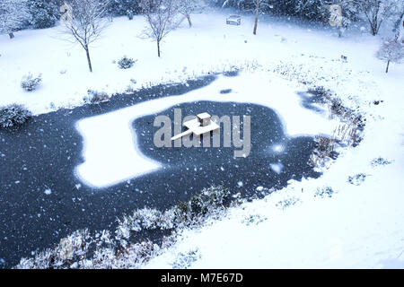 Scena di neve, la neve è caduta su un Duck Pond con un anatra casa e ghiaccio, intorno al laghetto è un grande giardino con alberi e un sedile in legno vi è t Foto Stock