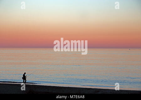 Un solitario mare pescatore pesci dalla spiaggia al tramonto, Benalmadena, Costa del Sol, Spagna Foto Stock