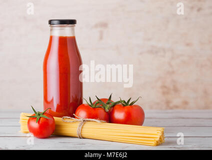 Bottiglia in vetro di concentrato di pomodoro a crudo con spaghetti e freschi pomodori organici su sfondo di legno Foto Stock