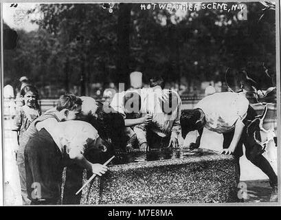 Questa scena di strada a New York cattura i bambini che si rinfrescano in una fontana durante il caldo. L'immagine riflette la vita urbana dei primi anni del XX secolo, mostrando come i bambini della città interagissero con gli spazi pubblici. Foto Stock