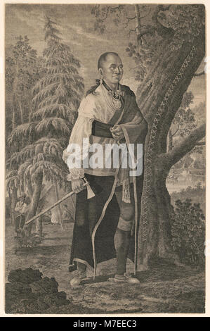 Un ritratto a figura intera di Hendrick, un capo Mohawk, in piedi con un tomahawk in mano e una scena di campo visibile sullo sfondo, raffigurante il suo ruolo nella leadership e nella cultura dei nativi americani durante il XVIII secolo. Foto Stock