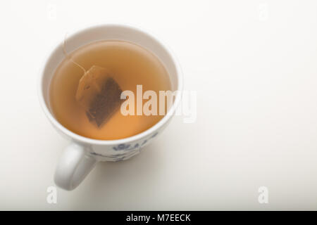 Bustine di The macerazione in acqua bollente in una tazzina durante la preparazione di rilassarsi sorseggiando una tazza di tè su uno sfondo bianco Foto Stock