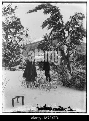 Questa fotografia del 1921 cattura due persone che camminano attraverso alberi innevati a Gerusalemme. La scena mette in evidenza la rara presenza di neve in città e offre uno scorcio della vita durante questo periodo in Medio Oriente. Foto Stock