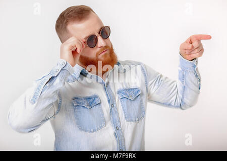 Sorridente i capelli rossi barba uomo in occhiali da sole e denim shirt rivolto lontano Foto Stock