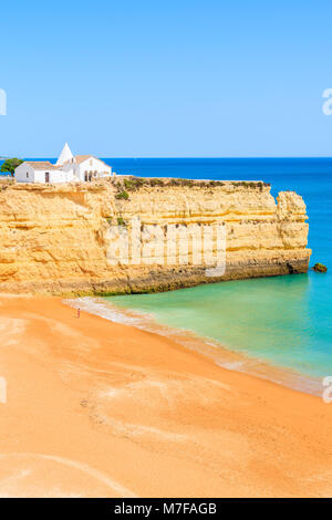 Vista della spiaggia con scogli di roccia e chiesa bianca in Armacao de Pera comune, Algarve, PORTOGALLO Foto Stock