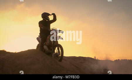 Professional Motocross Biker spettacolarmente sorge sulla duna fuoristrada sulla sua moto enduro. Guarda lontano su tutta la pista. Foto Stock