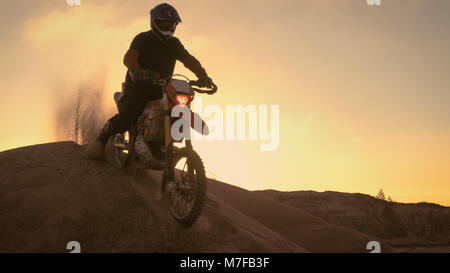 Professional Motocross Moto Rider drive sulle dune e si ferma sulla parte superiore. È il momento del tramonto e la via è coperto con fumo/ nebbia. Foto Stock