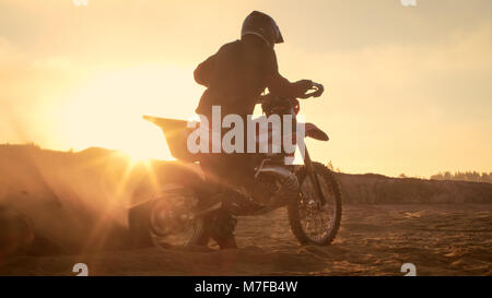 Professional FMX Motociclista torsioni pieno impugnatura a farfalla e inizia a correre sulla spiaggia sabbiosa di Off-Road via. Scenic tramonto. Foto Stock