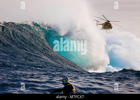 Un elicottero filmare un tow-in surfer a Peahi (ganasce) off Maui. Hawaii. La testa in primo piano è alla guida di un jetski. Foto Stock