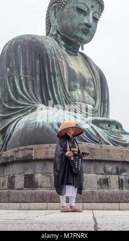 Buddista Giapponese pellegrino nel cappello di paglia black robes e pantaloni bianchi il canto dei sutra lo squillo di campana e azienda nero laccato campana sopraffatte da Buddha Foto stock Alamy