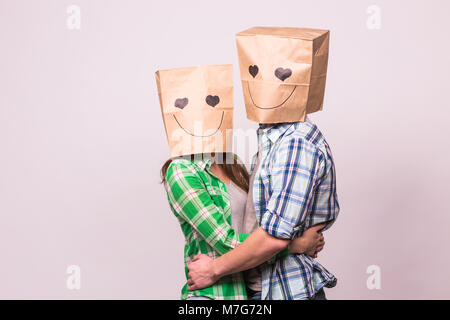 Amore giovane che coprono i loro volti con sacchetto di carta su sfondo bianco. Foto Stock