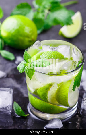 Il freddo estivo rinfrescante drink con calce, menta e cubetti di ghiaccio in un bicchiere su una pietra scura sullo sfondo. Il mojito. Limonata. Detox. Acqua minerale. Selective fo Foto Stock