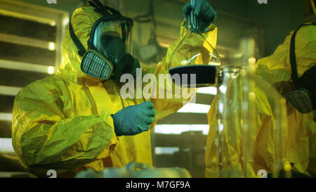In metropolitana farmaco Team di laboratorio dei farmacisti clandestino sintetizza le droghe illegali, uno detiene il becher con sostanze chimiche e controlli di coerenza Foto Stock