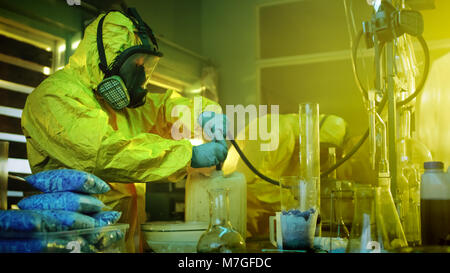 In metropolitana farmaco due laboratori chimici clandestino indossando maschere protettive e tute usare tubo flessibile per distillazione del farmaco. Cucinano met. Foto Stock