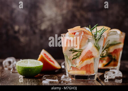 Bicchieri di acqua ghiacciata con agrumi e rosmarino servita su un tavolo di legno. Foto Stock