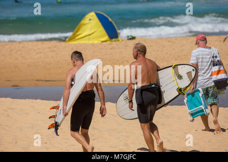 Due uomini maschi che trasportano le loro tavole da surf sul Nord Curl Curl Beach a Sydney, Australia Foto Stock