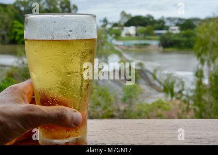 Bere una birra con vedute di acqua traboccante il weir dopo i recenti heavy rain, Riverview Tavern di Douglas Townsville Queensland Australia Foto Stock