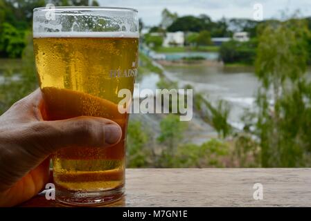 Bere una birra con vedute di acqua traboccante il weir dopo i recenti heavy rain, Riverview Tavern di Douglas Townsville Queensland Australia Foto Stock