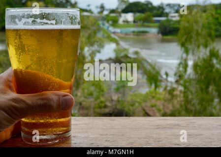 Bere una birra con vedute di acqua traboccante il weir dopo i recenti heavy rain, Riverview Tavern di Douglas Townsville Queensland Australia Foto Stock