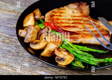 Controfiletto alla griglia bistecche con funghi e asparagi verdi su di una piastra di messa a fuoco selettiva, primo piano Foto Stock