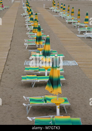 Giallo e verde di sedie a sdraio e ombrelloni disposti lungo una spiaggia italiana Foto Stock