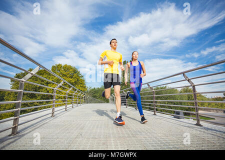 Basso angolo vista della giovane coppia fitness in sport vestito in esecuzione attraverso un ponte Foto Stock