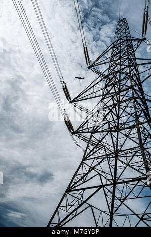 Basso angolo di visione di un aeroplano che vola al di sopra di un traliccio di elettricità nel Hertfordshire REGNO UNITO contro un sfondo nuvoloso Foto Stock