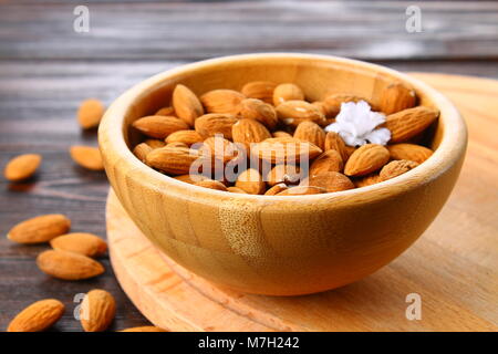 Materie frutta secca di mandorle in una ciotola di legno su una tavola di legno Foto Stock