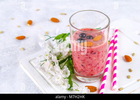 Mirtillo frullati di frutti di bosco, banana e mandorle in bicchieri con cocktail di tubi su un bianco tavola di legno Foto Stock