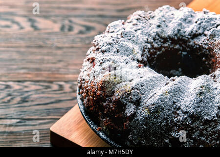 Deliziosi piatti fatti in casa torta al cioccolato con ciliegie e wallnuts decorata con zucchero in polvere su di un tagliere di legno su rustico backgroun vintage Foto Stock