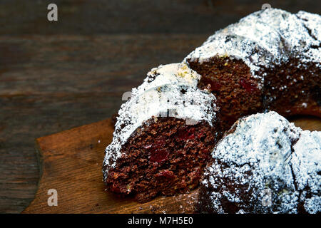 Deliziosi piatti fatti in casa torta al cioccolato con ciliegie e wallnuts decorata con zucchero in polvere su di un tagliere di legno su sfondo rustico, selezione Foto Stock